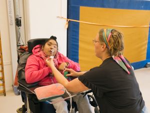 Persoon in rolstoel blaast bellen door een bellenblazer die een ander persoon voor de mond houdt