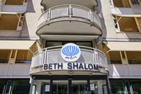 Ingang van het Beth Shalom-gebouw met een balkon erboven en een blauw-wit embleem met Hebreeuwse tekst op de gevel.