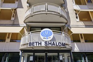 Ingang van het Beth Shalom-gebouw met een balkon erboven en een blauw-wit embleem met Hebreeuwse tekst op de gevel.