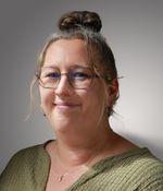 Een vrouw met blond haar in een knot, een bril en een neuspiercing kijkt vriendelijk in de camera