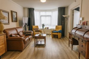 Lichte woonkamer van een appartement, met een erker. Ingericht met een leren bank, 2 gele fauteuils, een dressoir.