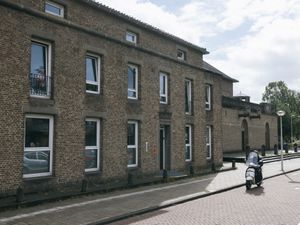 Een bruin historisch gebouw met drie verdiepingen en witte kozijnen. Daarnaast is een deel van een gebouw zichtbaar dat lijkt op een kerk.