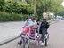 Jonge man met kort zwart haat zit met een grote lach naast een begeleider met blonde paardenstaart p een duo-fiets.