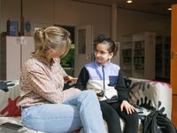 Verpleegkundige en kind zitten op een bank en kijken naar elkaar