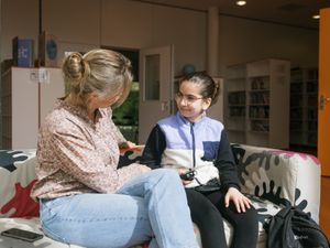 Verpleegkundige en kind zitten op een bank en kijken naar elkaar