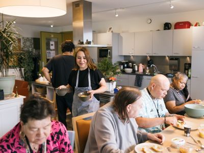 4 mensen eten de maaltijd met elkaar en iemand brengt schaaltjes met eten aan tafel