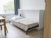 Een slaapkamer met bed dat je vanuit de muur naar beneden kunt klappen. Op het bed ligt een gekleurde, gehaakte deken.