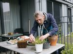 Persoon is buiten diens appartement plantjes aan het verpoten op een tuintafel