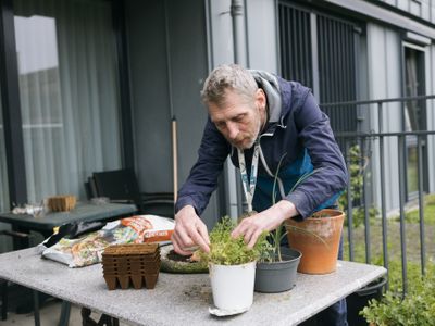 Persoon is buiten diens appartement plantjes aan het verpoten op een tuintafel