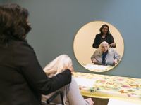 1 persoon doet een blauw-rood-geel gestreepte band in het haar van de ander voor de spiegel