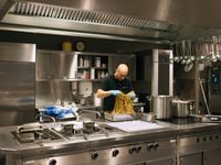 Een kale man met zwart Cordaan shirt maakt spaghetti in een grote restaurantkeuken.