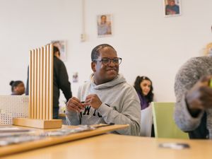 Persoon is in ruimte voor dagbesteding met andere mensen en zit aan tafel achter spel en wacht om hiermee te beginnen