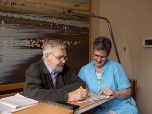 Oudere meneer en medewerkster maken samen een kruiswoordpuzzel