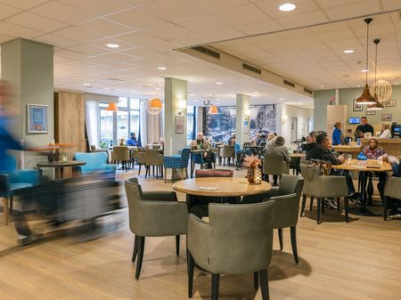 Gezellige lichte restaurantruimte met bar en ronde tafels en leren groengrijze stoelem