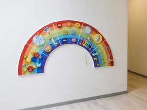 Een houten regenboog bevestigd aan een witte muur met daaraan allerlei kleine spelletjes en instrumenten om mee te spelen.