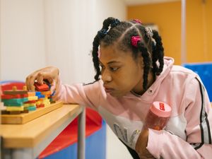 Meisje met veel staartjes houdt roze drinkbeker vast en doet een spelletje