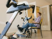 Oudere dame zit fietst vanuit haar stoel in fitnessruimte