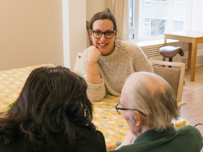 Persoon zit aan tafel in gesprek met 2 personen