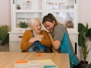 Oudere dame en medewerkster zitten aan tafel en lachen samen