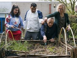 4 personen maken een moestuinbak, die op kniehoogte staat, vuilvrij met handharkjes
