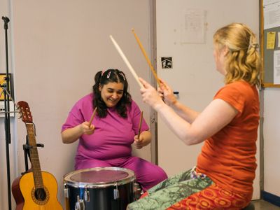 Muziektherapeut en dame met donker haar in staartjes hebben plezier in het samen drummen op 1 drumstel