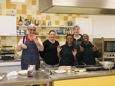 5 personen waarvan 2 begeleiding staan lachend in de keuken bij versgebakken koekjes