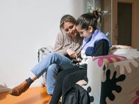 Verpleegkundige en kind zitten op een bank en kijken naar apparaatje in kinds hand