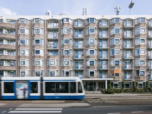 Licht gebouw met 6 verdiepingen met veel erkers. De ingang aan de stoep. Op de voorgrond komt een tram voorbij.