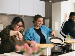 Twee dames van rond de dertig bakken pannenkoeken en kijken er blij bij