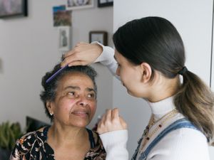 Verzorgende met lange bruine paardenstaart kamt het haar van een oudere dame