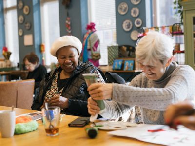 Twee oudere dames zitten aan tafel te schilderen en lachen