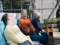 3 personen zitten op een bank in de tuinkas met elkaar van de zon te genieten