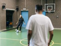 Jonge vrouw met blond haar met sportieve kleding en een grote lach op haar gezicht trapt tegen een voetbal met sterren in een gymzaal