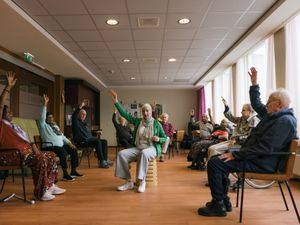 Groep ouderen zit in een kring op een stoel te bewegen met medewerker in het midden