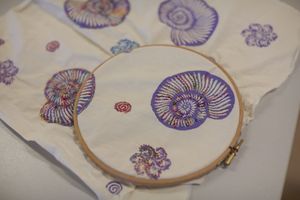 Een borduurring met daarin stof met paarse schelpenprint en gekleurde draad.