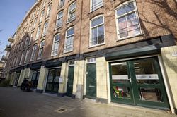 Straatbeeld van bakstenen gebouwen met grote groene ramen en deuren, met een winkelpui waarop een SamSam-sticker staat.