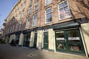 Straatbeeld van bakstenen gebouwen met grote groene ramen en deuren, met een winkelpui waarop een SamSam-sticker staat.