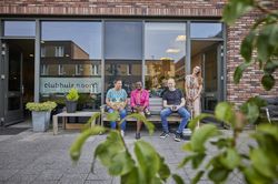 Vier mensen zitten gezellig buiten op een bankje bij Clubhuis Noord. Ze genieten van het zonnetje.