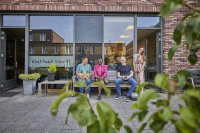 Vier mensen zitten gezellig buiten op een bankje bij Clubhuis Noord. Ze genieten van het zonnetje.