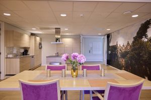 Moderne keuken-eetkamer met een tafelstuk van roze bloemen, paarse stoelen, houten keuken en een sfeervolle fotowand.