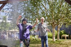 2 personen staan lachend en zwaaiend met de handen bij de tuinsproeier in de tuin