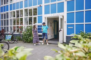 Een geanimeerd gesprek tussen een begeleider en een deelnemer voor de ingang van Centrum Kijkduin.