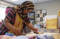 Een donkere vrouw met hoofddoek is geconcentreerd bezig met het knippen van een stuk stof.