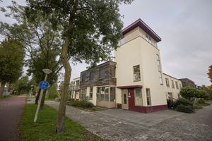 Modern hoekgebouw met een witte toren en rijtjeshuizen met houten bekleding, een fietspadbord en bomen op de stoep.