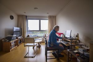 Een man zit in zijn appartement achter zijn computer. In de kamer liggen veel cd's en er is een geluidsinstallatie.