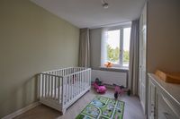 Kinderkamer met wit bedje, speelkleed, roze speelgoedauto en -step bij het raam en verschoontafel.