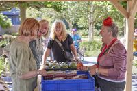 Medewerker, vrijwilligers en buurtbewoner staan bij voedseluitgifte buiten onder overkapping