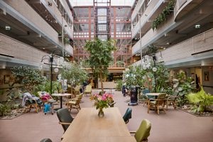 Een ruim overdekt atrium met planten, zitgelegenheid en een centrale houten tafel versierd met bloemen, verlicht door natuurlijk daglicht.
