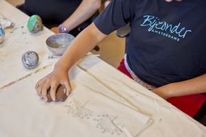 Iemand met een donkerblauw shirt met de tekst 'Bijzonder Amsterdams' stempelt een afdruk van een bloem op een stuk stof.