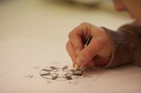 Een hand met potlood tekent een ster met versiering op papier.